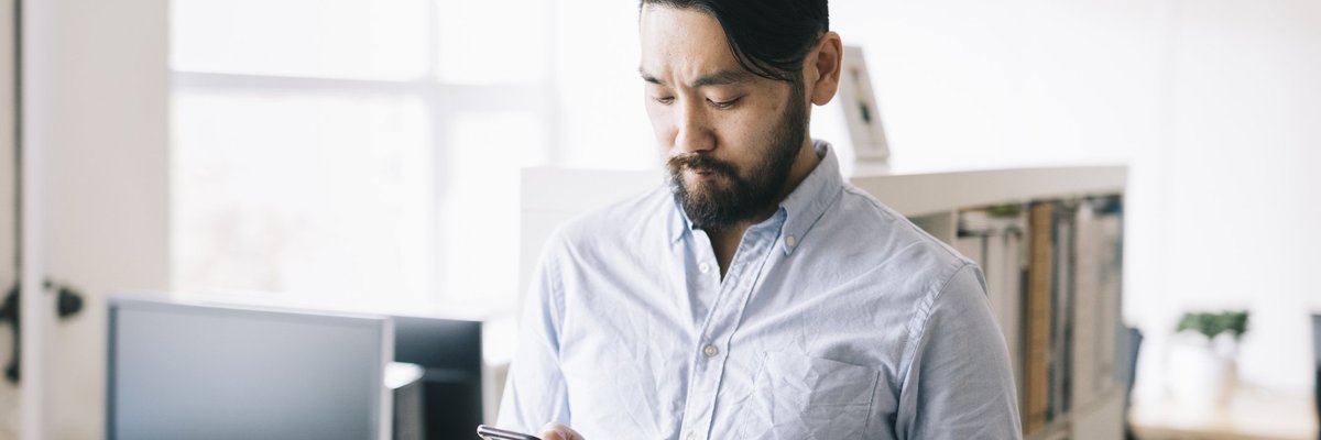 A man standing in an office while holding his phone and a credit card.