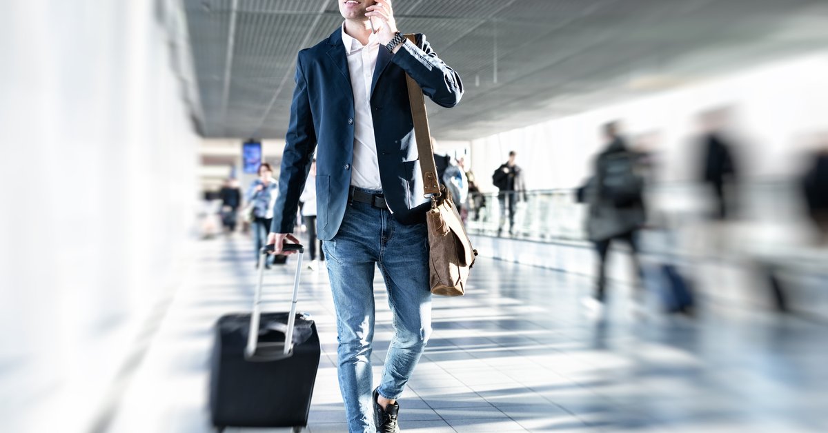 man in airport with suitcase and on the phone 