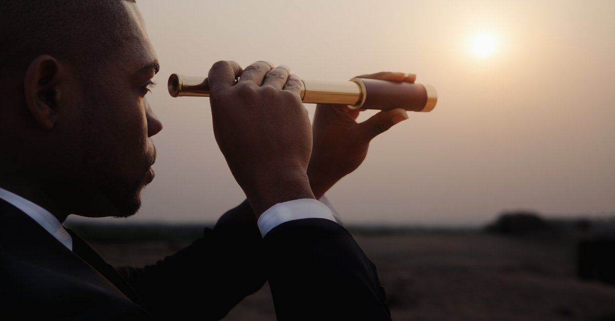 man in business suit looking through telescope toward horizon.