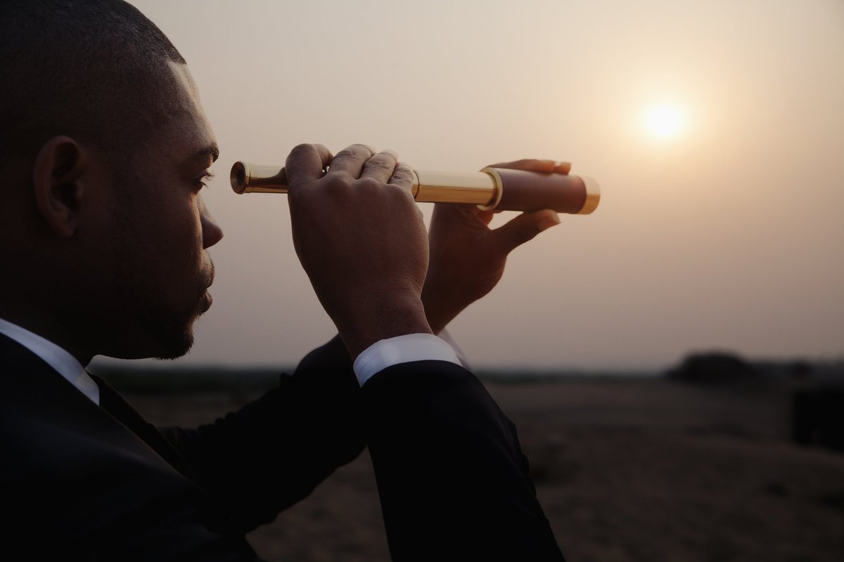 man in business suit looking through telescope toward horizon.