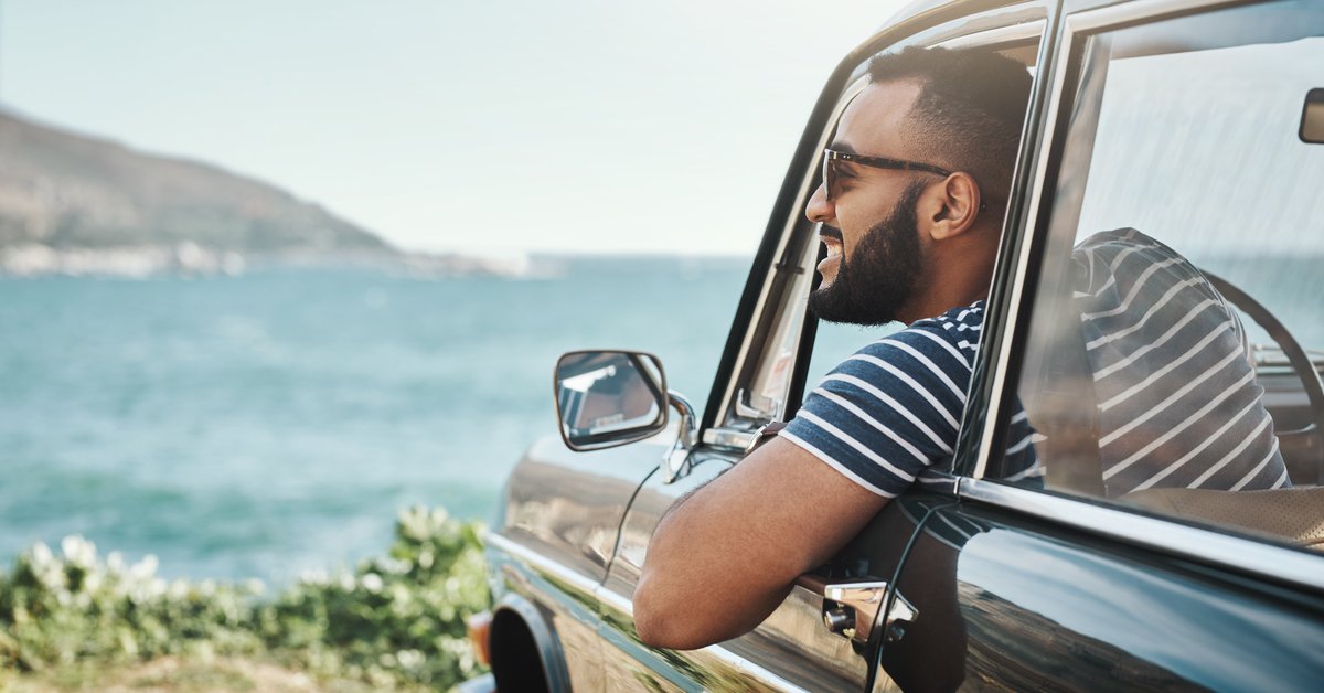 A happy man leaning out of his car window and taking in the view of the ocean.