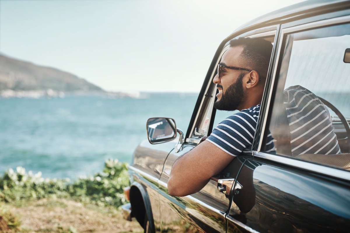 A happy man leaning out of his car window and taking in the view of the ocean.