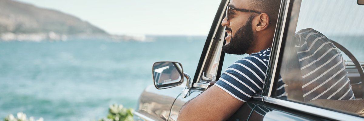 A happy man leaning out of his car window and taking in the view of the ocean.