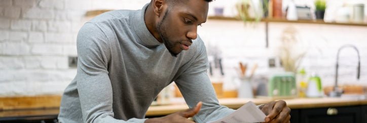 A man leaning against his kitchen counter while opening the mail.