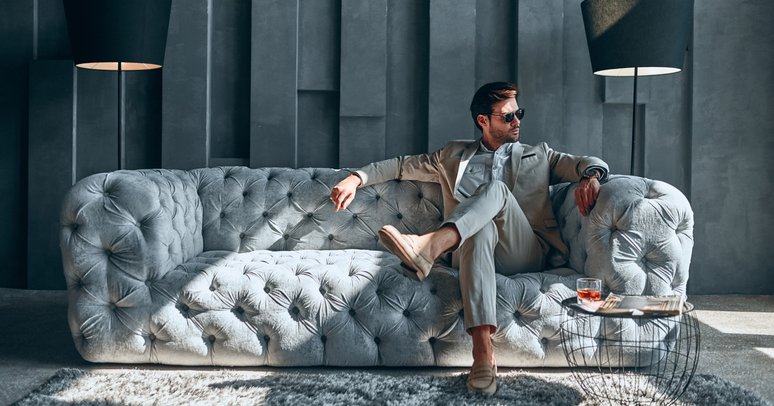 A stylishly dressed man sitting on an expensive-looking couch in a lavishly decorated room.