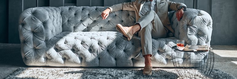 A stylishly dressed man sitting on an expensive-looking couch in a lavishly decorated room.