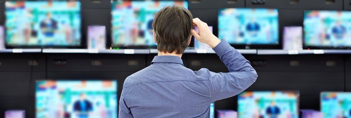 A man standing in front of a wall of TVs in an electronics store.