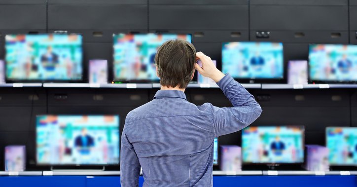 A man standing in front of a wall of TVs in an electronics store.