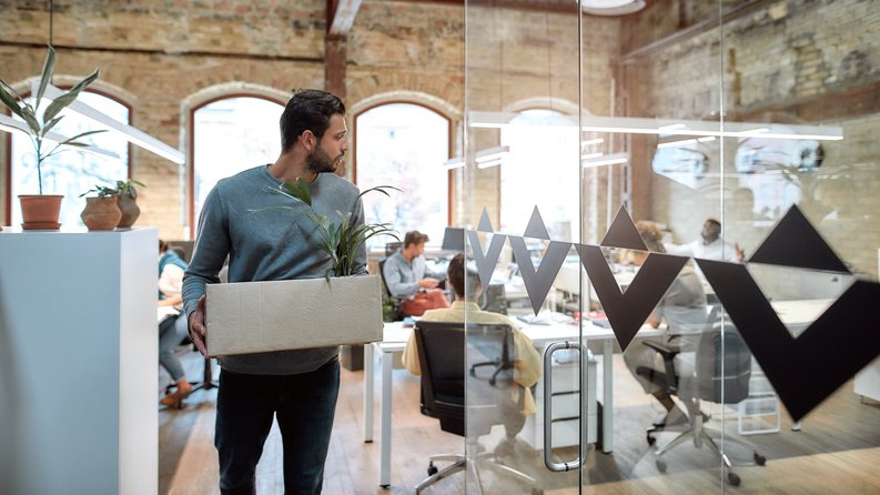A man walking out of an office with box of his things after being let go.