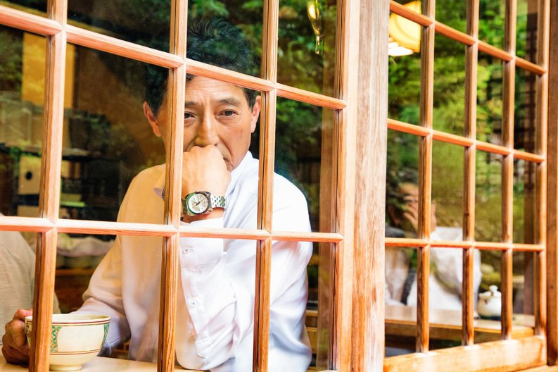 A man looking pensively out the window of a cafe while drinking tea.