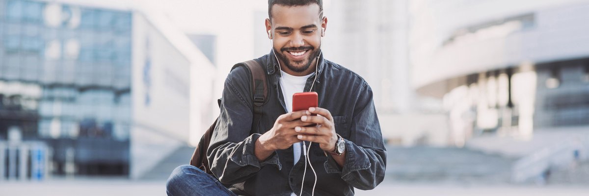 A man texting on his cell phone while sitting in an outdoor square between buildings.