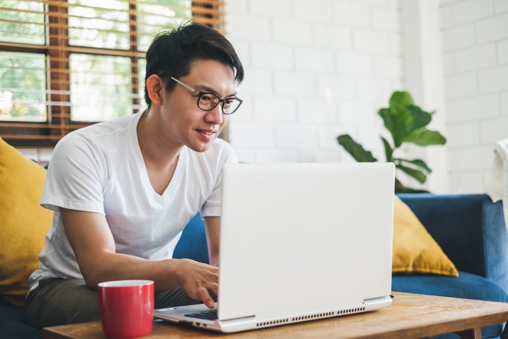 A man sitting on his couch at home and typing on his laptop on the coffee table.