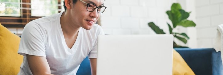 A man sitting on his couch at home and typing on his laptop on the coffee table.