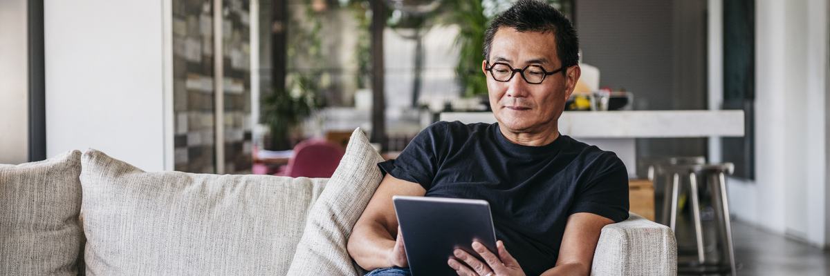 A man sitting on his couch and reading on a tablet.