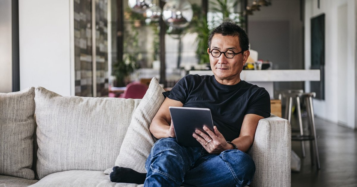A man sitting on his couch and reading on a tablet.
