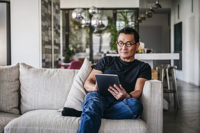 A man sitting on his couch and reading on a tablet.