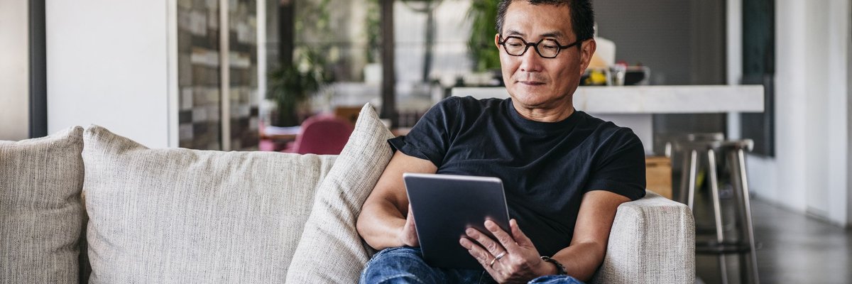 A man sitting on his couch and reading on a tablet.