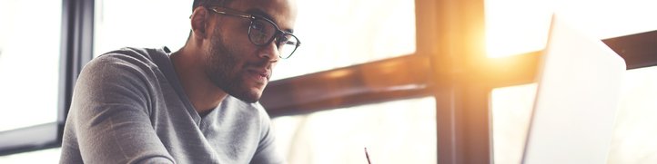 A man concentrating on his laptop while sitting next to a sunny window.