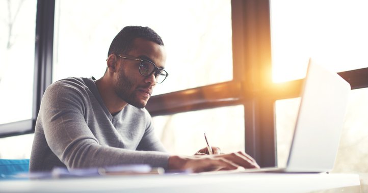 A man concentrating on his laptop while sitting next to a sunny window.