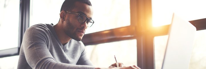 A man concentrating on his laptop while sitting next to a sunny window.
