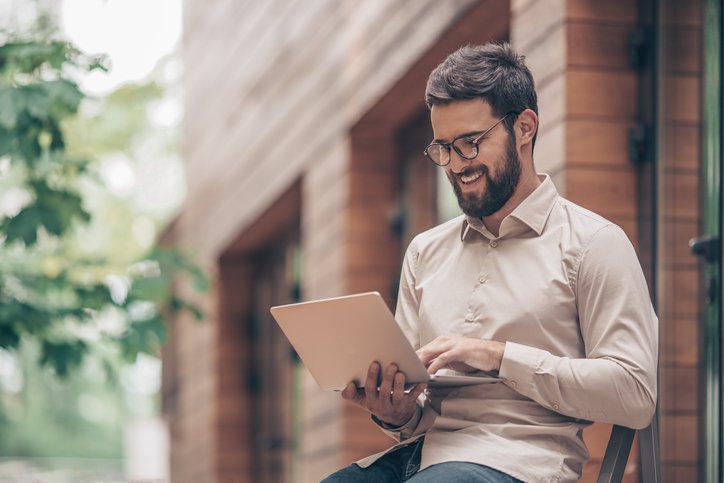 A man typing on his laptop while sitting outside in front of a brick building.