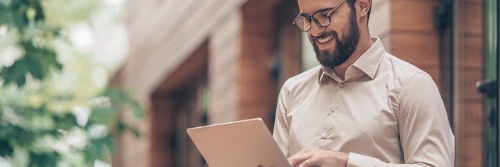 A man typing on his laptop while sitting outside in front of a brick building.