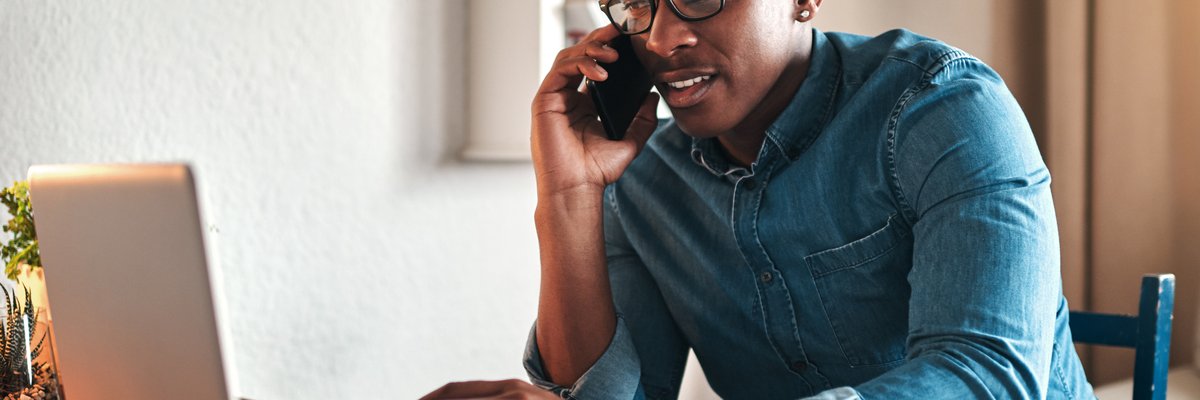 A man on a phone call while sitting in front of his laptop.