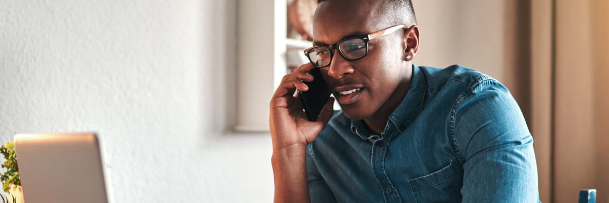 A man on a phone call while sitting in front of his laptop.