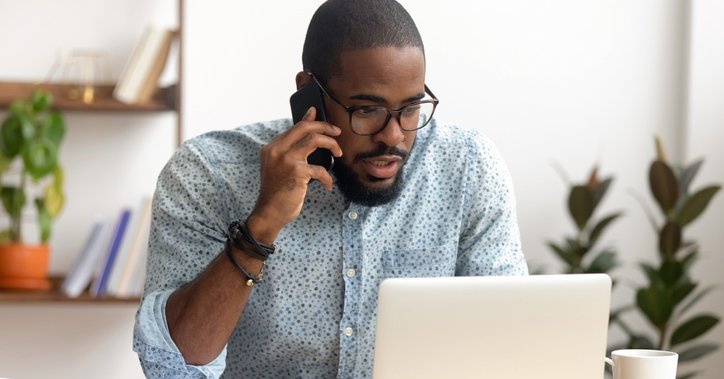 A man sitting in front of his laptop at home and making a phone call.