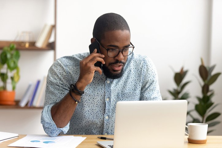 A man sitting in front of his laptop at home and making a phone call.