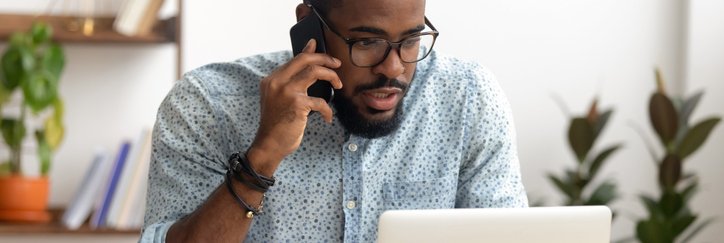 A man sitting in front of his laptop at home and making a phone call.