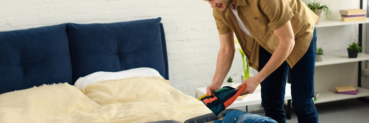 A man packing a suitcase that's sitting open on a bed.
