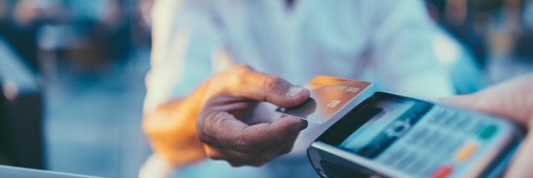 A man holding his credit card over a card payment reader.