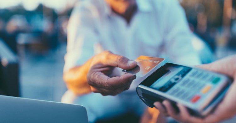 A man holding his credit card over a card payment reader.