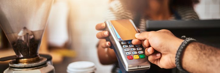 A man using a touchless reader that a barista is holding to pay with his credit card at a cafe.