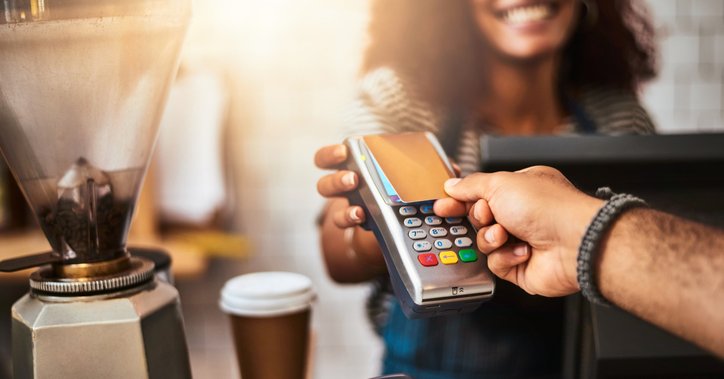 A man using a touchless reader that a barista is holding to pay with his credit card at a cafe.