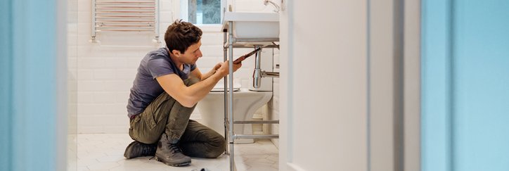 A man crouching on the floor next to tools while repairing a bathroom sink.
