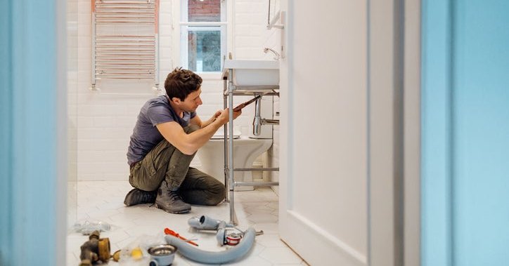 A man crouching on the floor next to tools while repairing a bathroom sink.