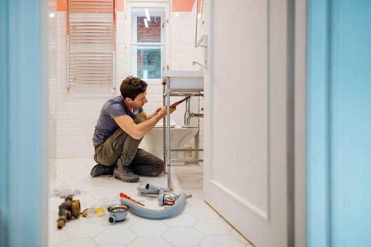 A man crouching on the floor next to tools while repairing a bathroom sink.