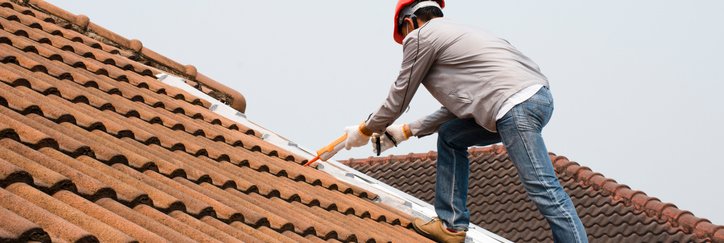 A man in a hard hat working on a tile roof.