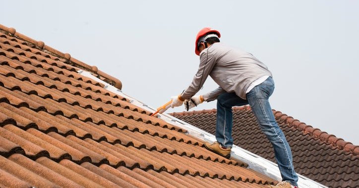 A man in a hard hat working on a tile roof.