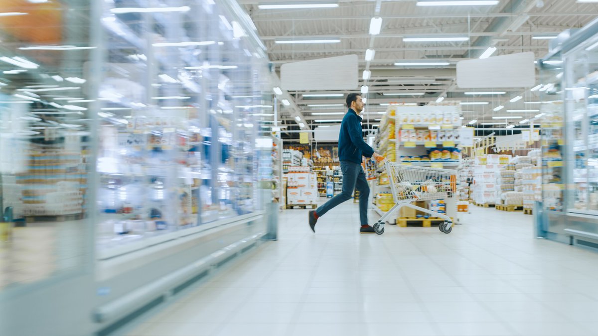 A man pushes a shopping cart through the aisles of a warehouse.