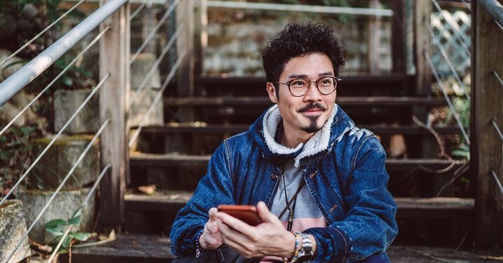 A man sitting on stairs in a park and holding a cell phone in his hand.