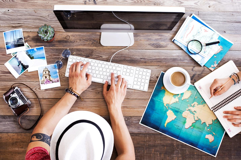 man typing on keyboard with camera, photos, and maps on desk