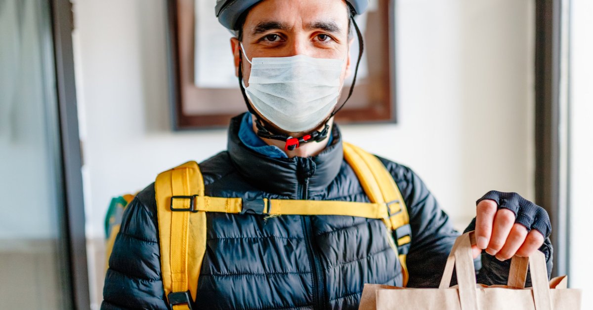 A man wearing a medical mask and delivering a bag of food.