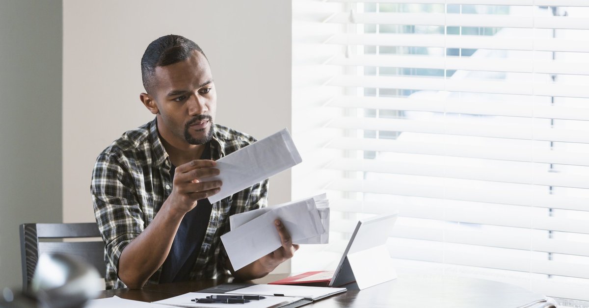 A man sitting at his dining table and opening a stack of bills.