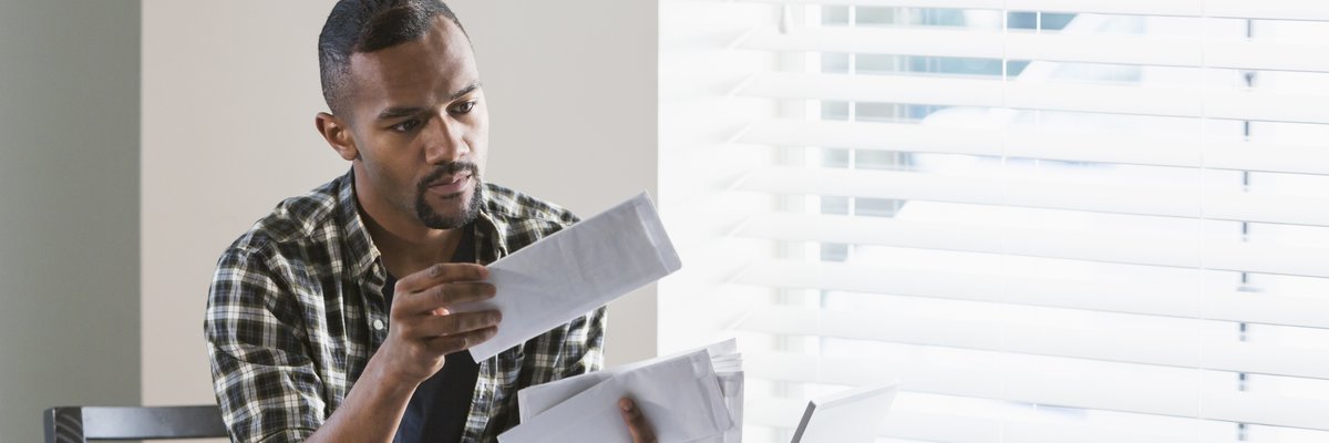 A man sitting at his dining table and opening a stack of bills.