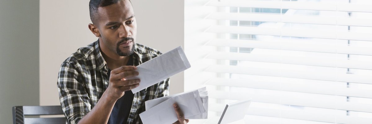 A man sitting at his dining table and opening a stack of bills.