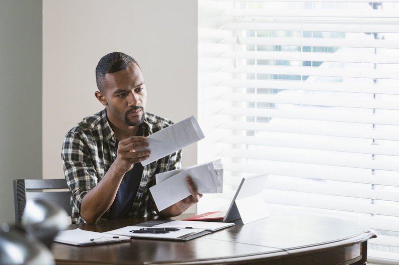 A man sitting at his dining table and opening a stack of bills.