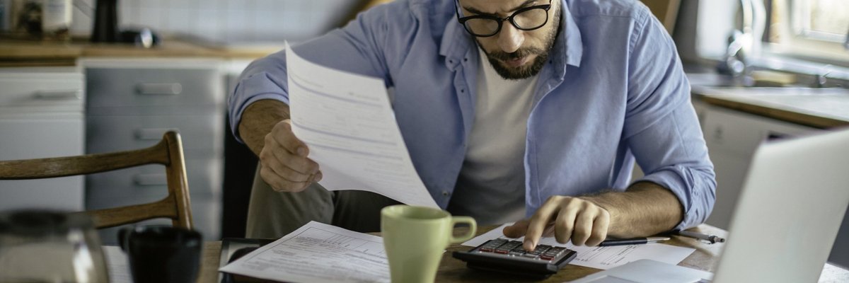 A man sitting at his kitchen table with a calculator and bills.
